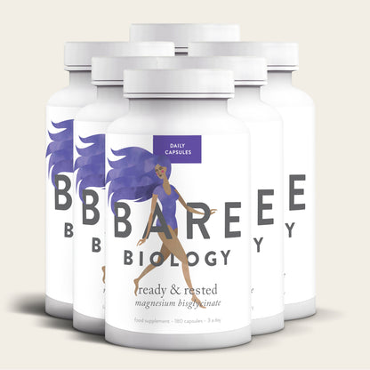 Five bottles of Bare Biologys Magnesium Glycinate Capsules are shown, labeled ready & rested with magnesium bisglycinate for easy absorption. The labels feature an illustration of a woman with flowing purple hair, symbolizing a calm and nourished nervous system.